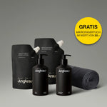 Jungkraut Körperpflege-Set bestehend aus Wild Forest Body Lotion und Mountain Rain Shower Gel in eleganten schwarzen Pumpflaschen sowie passenden Refill-Beuteln dahinter. Rechts liegt ein zusammengerolltes, dunkles Mikrofaserhandtuch. Ein gelber Kreis mit Text hebt hervor: GRATIS Mikrofasertuch im Wert von 30.–. Das Bild vermittelt hochwertige, nachhaltige Pflege mit modernem Design.