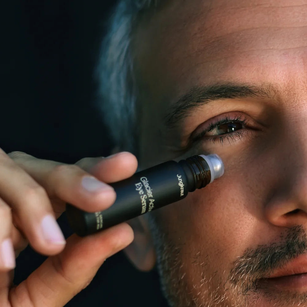 Nahaufnahme eines Mannes, der das Jungkraut Glacier Active Eye Serum mit einem Roll-on-Applikator unter dem Auge aufträgt. Das Bild vermittelt Pflege, Frische und Präzision bei der Anwendung der Augenpflege.