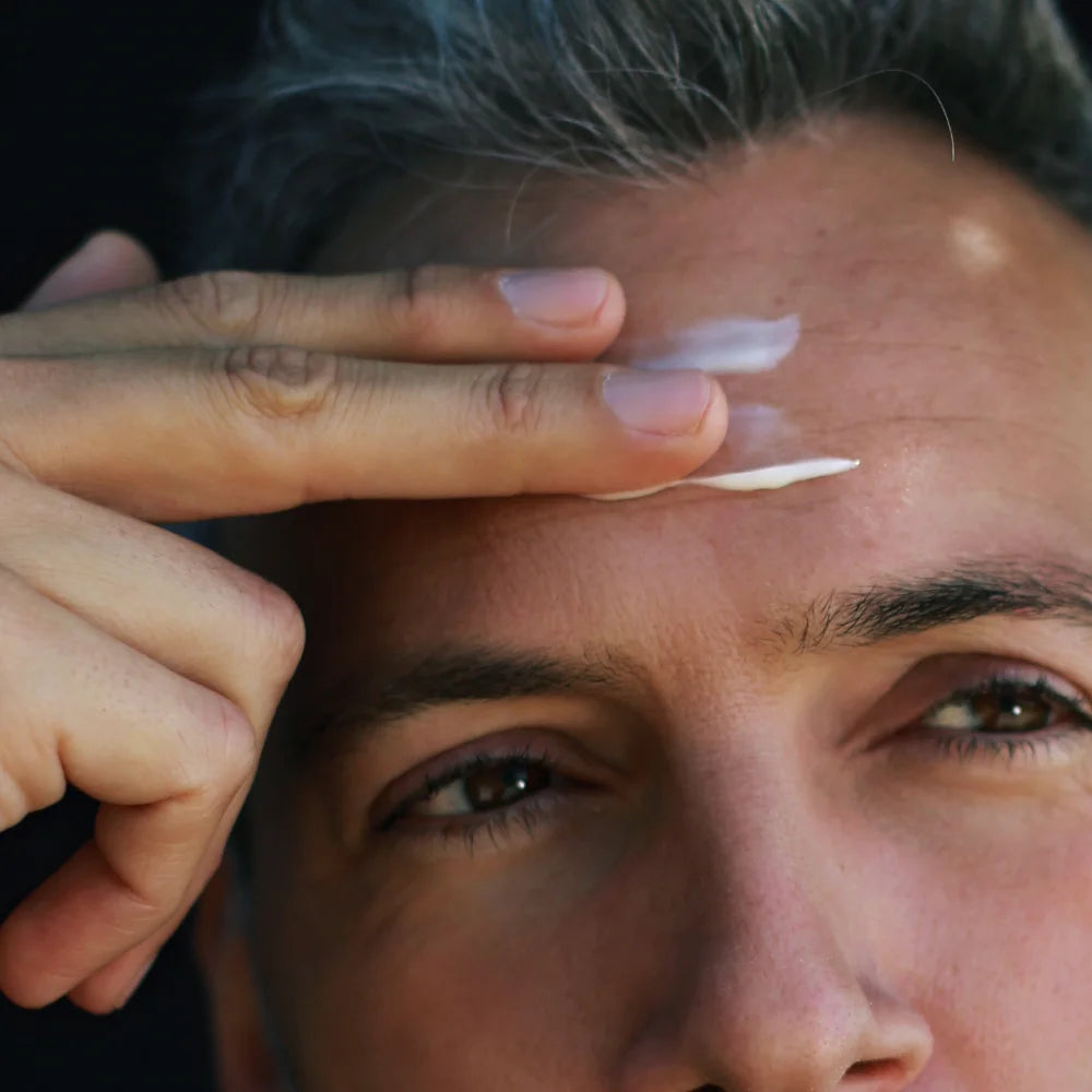 Nahaufnahme eines Mannes, der eine kleine Menge Gesichtscreme mit zwei Fingern auf seine Stirn aufträgt. Das Bild zeigt den Anwendungsschritt der Jungkraut Pflege – sanft, präzise und wohltuend für die Haut.